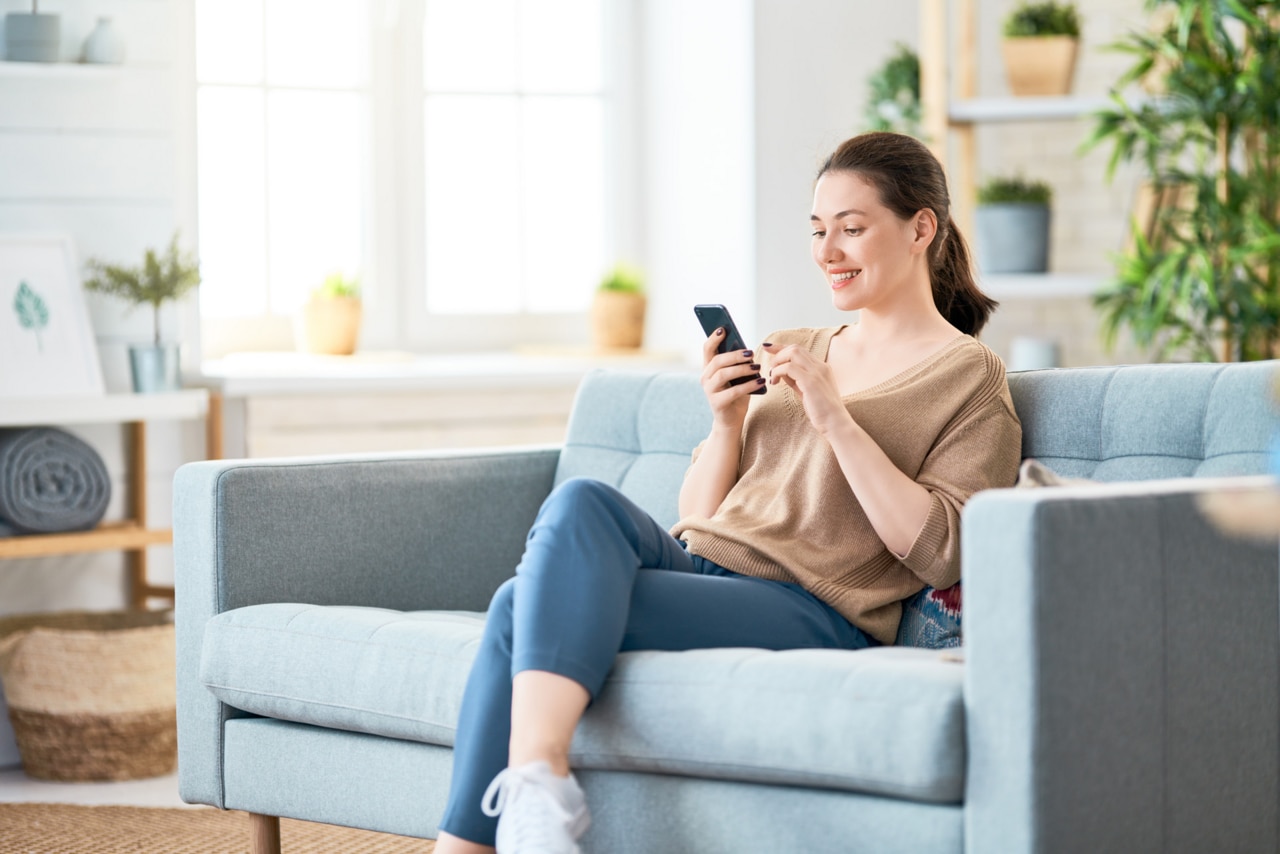 Happy casual beautiful woman is talking on a phone sitting on a sofa at home