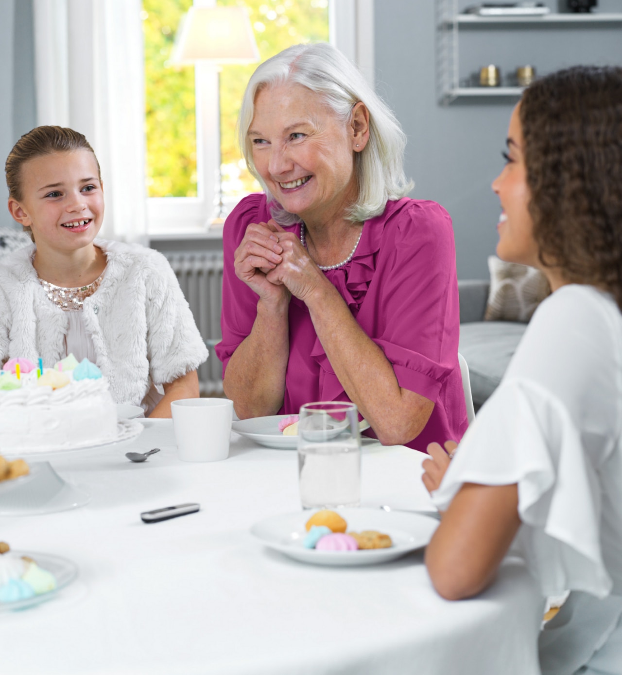 Grandmother with her two granddaughters sitting at a table - Phonak Roger on microphone in front of them placed on a table.