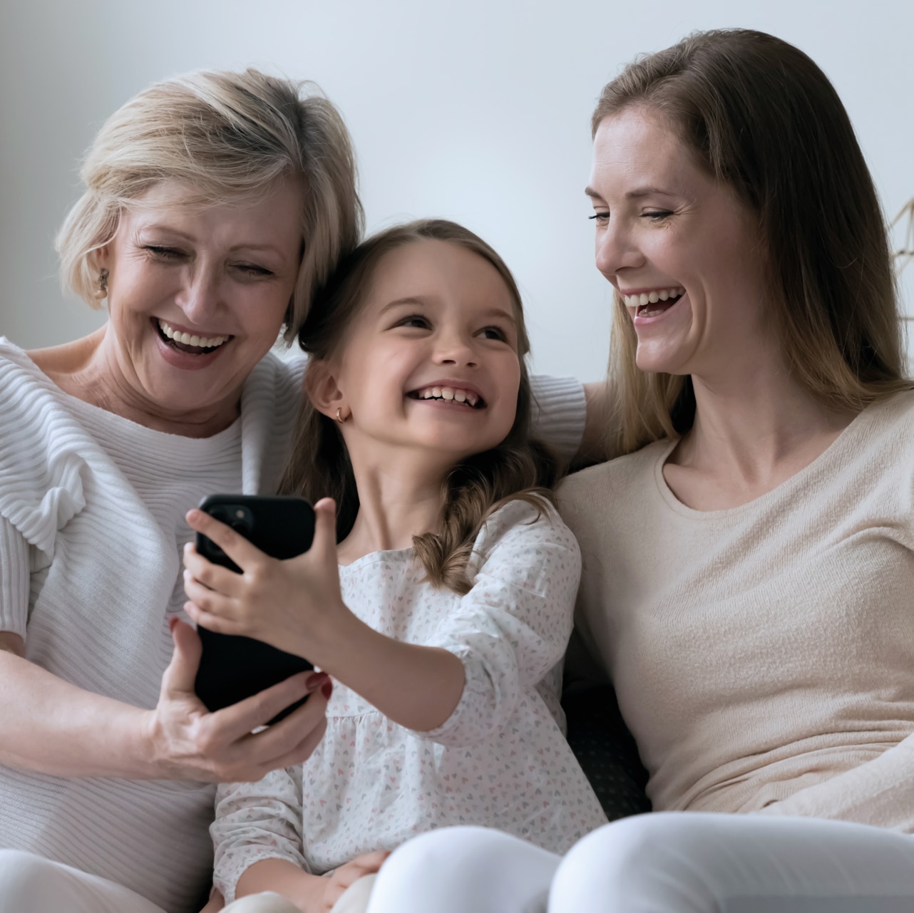 Mom, daughter and grandma sitting on the couch, looking at the phone screen and smiling.